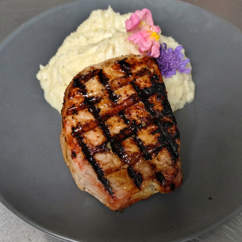 Grilled salmon fillet with crosshatch marks served alongside mashed potatoes and colorful edible flowers on a dark plate.