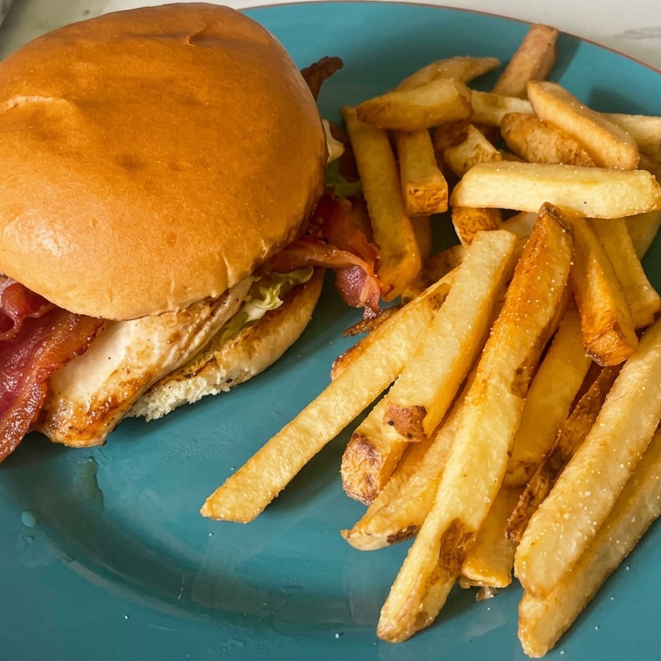 Bacon burger with lettuce on a toasted bun served alongside golden French fries on a teal plate.