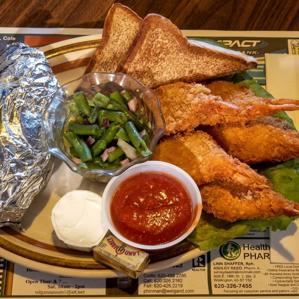 Plate of fried shrimp with toast, green beans, baked potato, tartar sauce, and red cocktail sauce on a restaurant table.